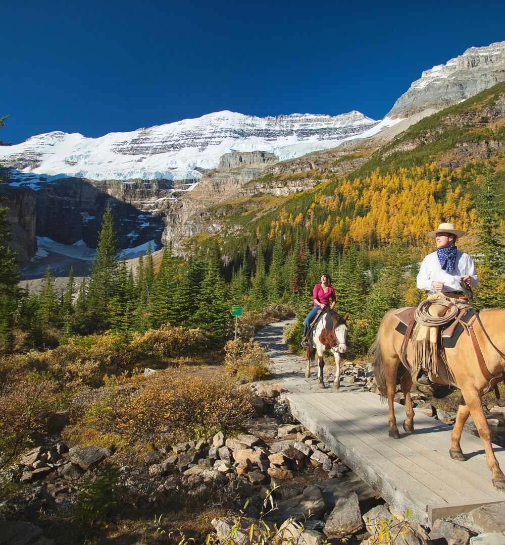 People on a guided horseback riding tour in Lake Louise with Victoria Glacier in the background